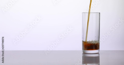 Cola pouring in a glass on a white reflective surface