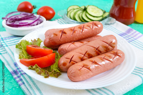 Delicious juicy grilled sausages on a plate, vegetables, ketchup and mustard on a bright background.