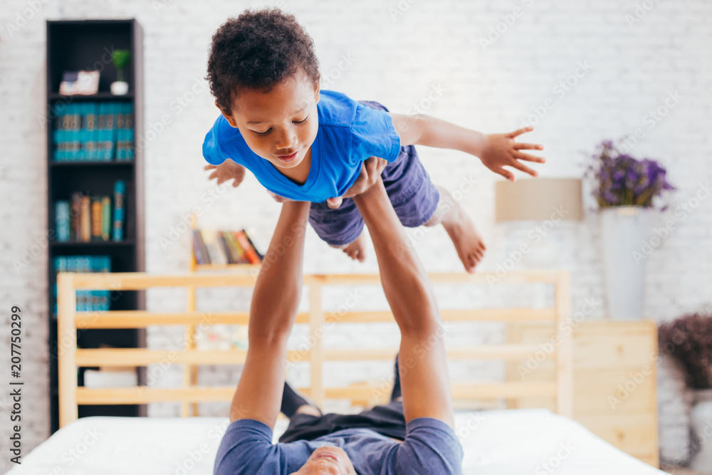 Φωτογραφία African American family of two, father lifting son up high on bed at home