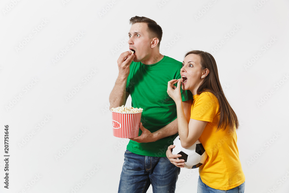 Shocked young couple, woman, man, football fans in yellow green t-shirt cheer up support team with soccer ball bucket of popcorn isolated on white background. Sport, family leisure, lifestyle concept Shocked young couple, woman, man, football fans in yellow green t-shirt cheer up support team with soccer ball bucket of popcorn isolated on white background. Sport, family leisure, lifestyle concept
