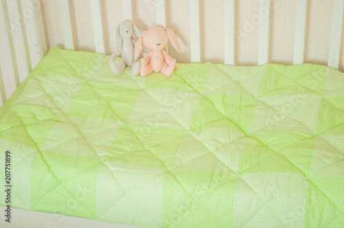 Baby bedding and quilted blanket in a white crib of tender lime green color