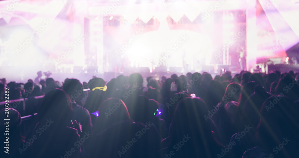 blurry of silhouettes of concert crowd at Rear view of festival crowd raising their hands on bright stage lights