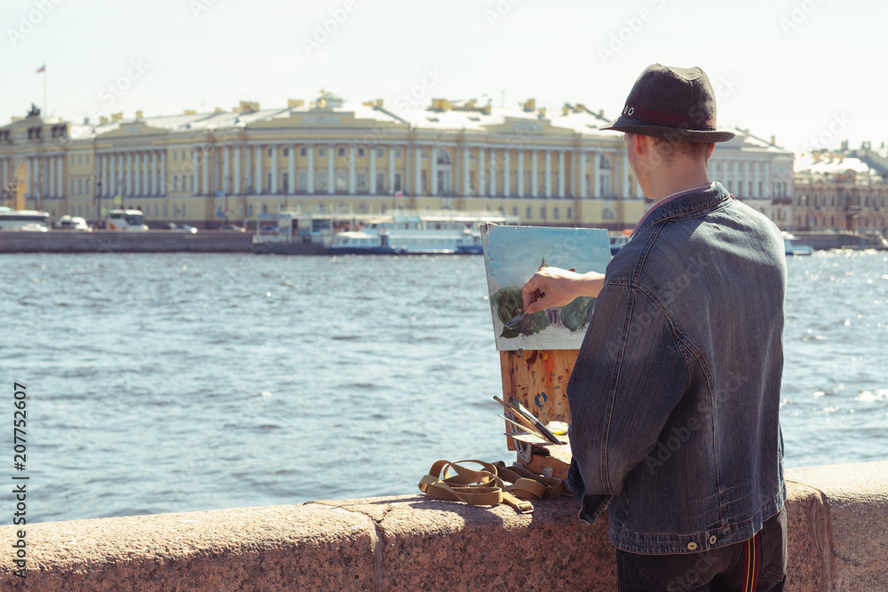 Young man in the hat is painting on waterfront