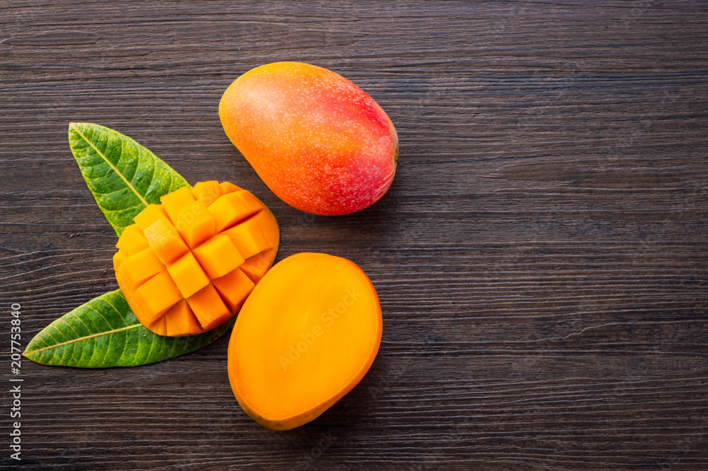 Fresh and beautiful mango fruit with sliced diced mango chunks on a dark wooden background, copy space(text space), blank for text, top view. Fresh and beautiful mango fruit with sliced diced mango chunks on a dark wooden background, copy space(text space), blank for text, top view.