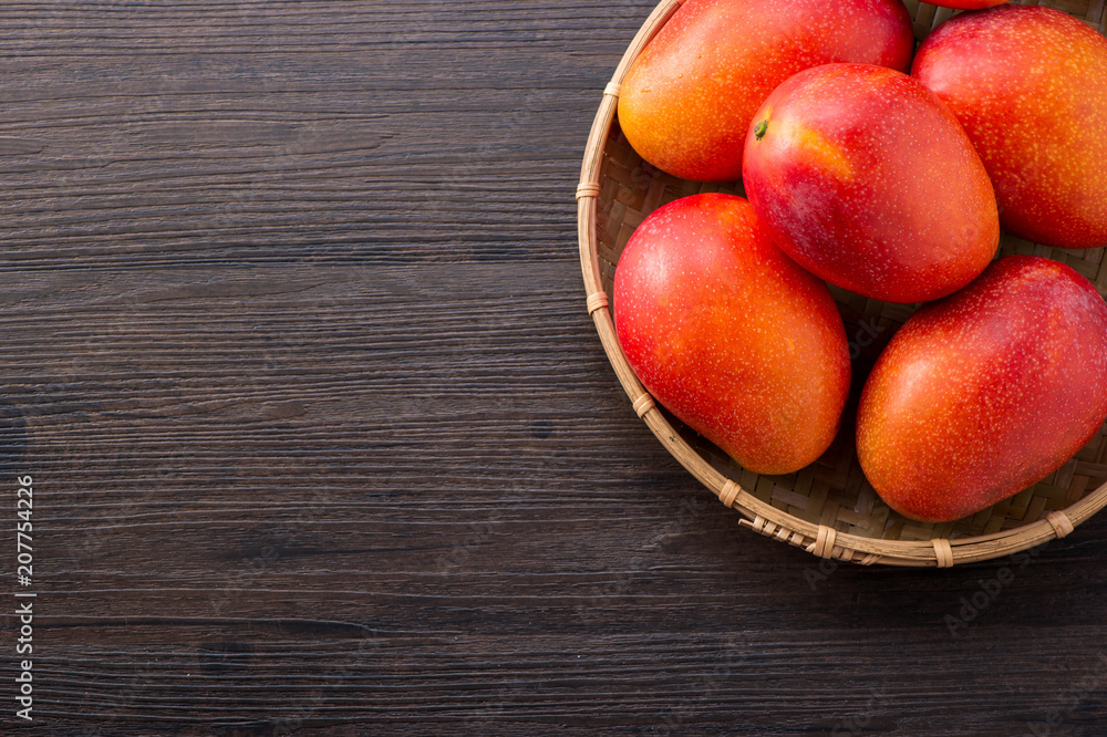 Fresh and beautiful mango fruit in a bamboo basket on a dark wooden background, copy space(text space), blank for text, top view. Fresh and beautiful mango fruit in a bamboo basket on a dark wooden background, copy space(text space), blank for text, top view.