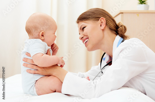 Smiling woman physician examining cute baby in the office. 