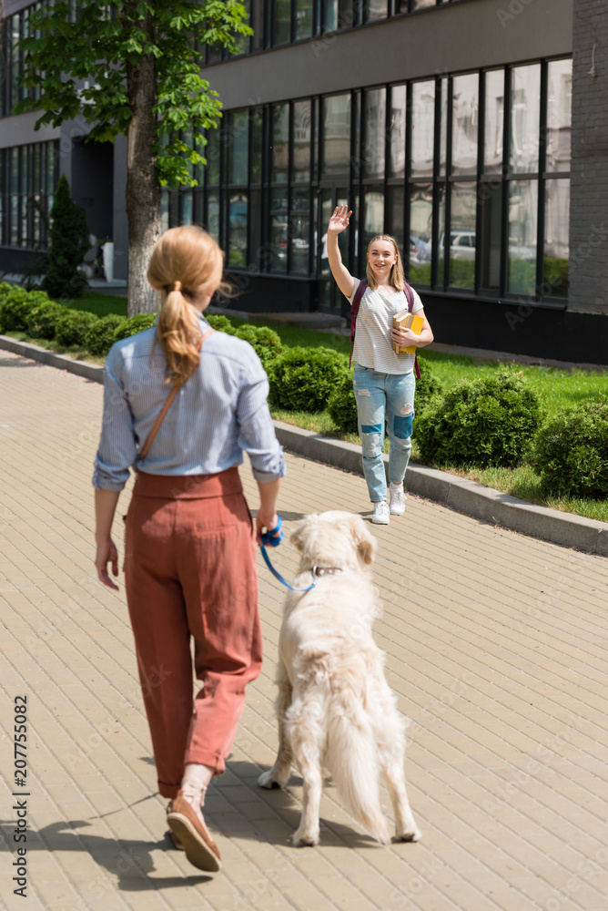 daughter waving to mother while she walking with dog on street daughter waving to mother while she walking with dog on street
