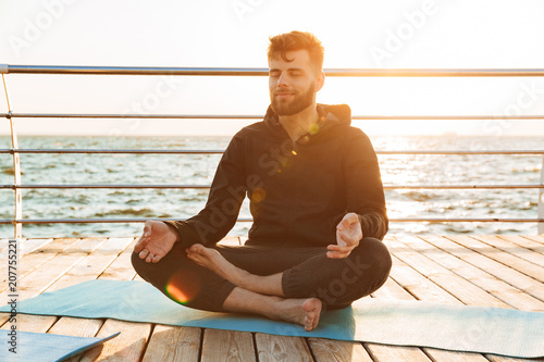 Relaxed young man meditating while sitting on a fitness mat