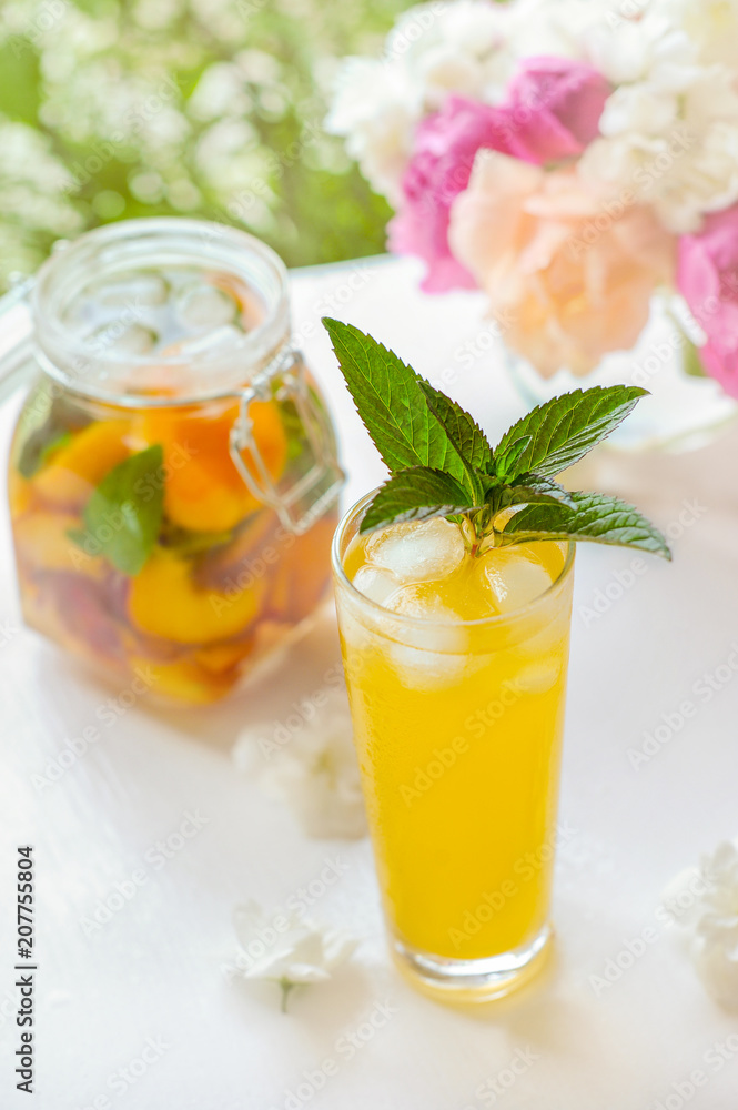 Pitcher with lid with water, detox with pieces of peach and apricot, with ice. A refreshing drink on a green background with a yellow rose. Pitcher with lid with water, detox with pieces of peach and apricot, with ice. A refreshing drink on a green background with a yellow rose.