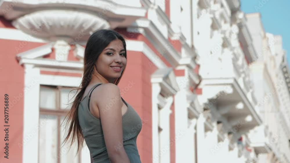 Portrait of young attractive girl turns and looks into the camera with smile. Woman with oriental face, brown eyes and stylish ombre dyed long hair on architecture city background. Portrait of young attractive girl turns and looks into the camera with smile. Woman with oriental face, brown eyes and stylish ombre dyed long hair on architecture city background.
