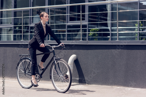 side view of young stylish businesswoman in suit riding retro bicycle