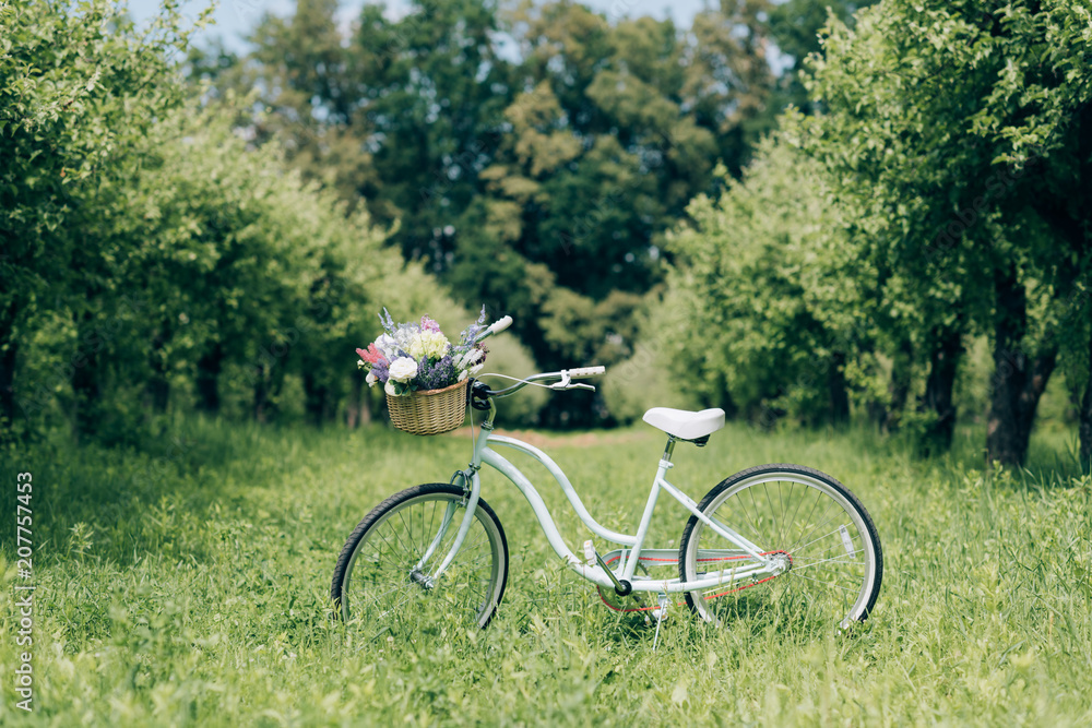 selective focus of retro bicycle with wicker basket full of flowers at countryside