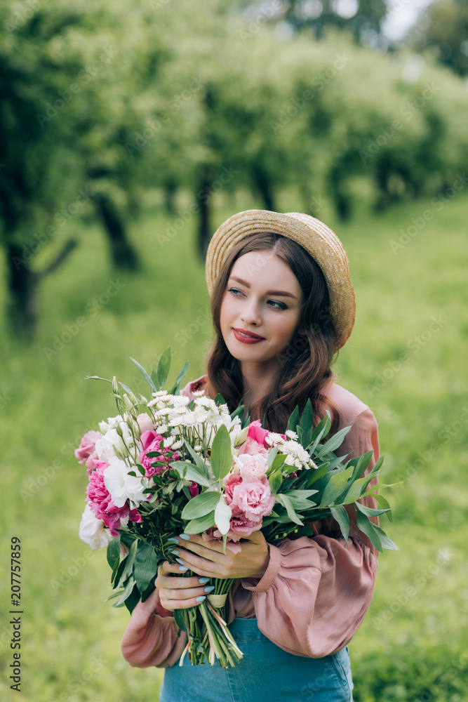 portrait of beautiful pensive woman in hat with bouquet of flowers in park