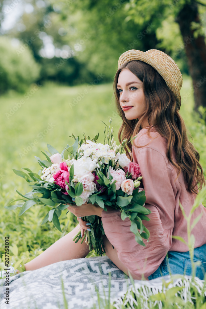 Fototapeta premium side view of beautiful pensive woman with bouquet of flowers resting on blanket in park