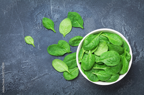 Green spinach leaves in bowl on black table top view. Organic and diet food.