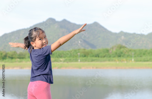 Happy kid with raised arms in lake and mountain.