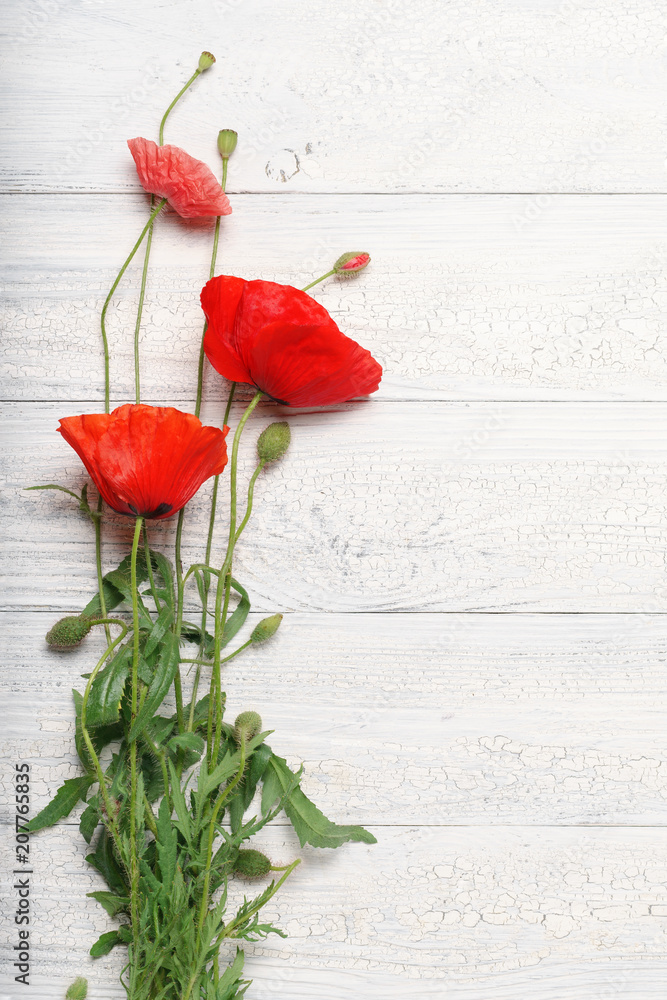 Fototapeta premium Czerwoni makowi kwiaty nad białą nieociosaną drewnianą powierzchnią.
