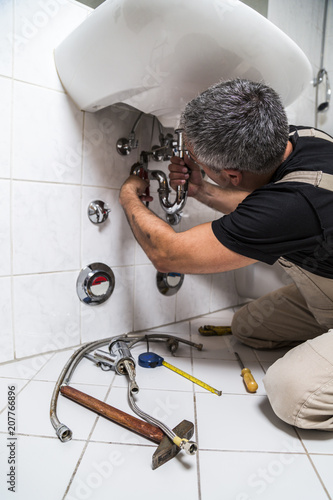 specialist male plumber repairs faucet in bathroom