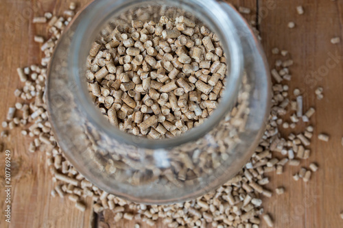 Wooden pet bedding in the glass jar standing on the plank. Wood pellets background.