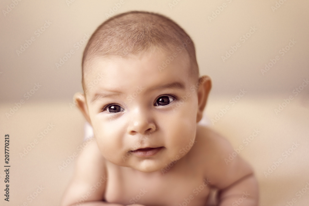 cute newborn baby girl lying on simple isolated beige background and looking at camera; childhood and innocence caoncept