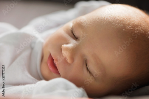 Sleeping infant newborn baby girl in white with closed eyes and long eyelashes; innocence
