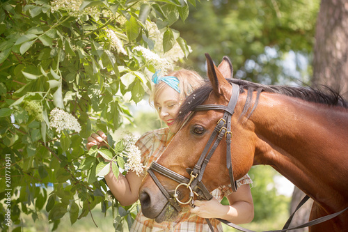 Cheerful, beautiful blonde girl walks in summer sunny weather in a forest by the river with a horse