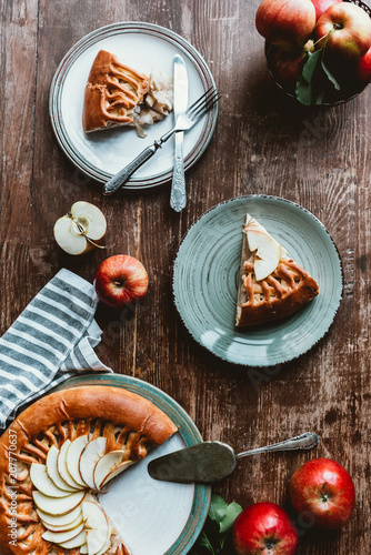flat lay with pieces of apple pie on plates, cutlery and fresh apples on wooden tabletop