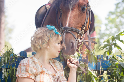 Cheerful, beautiful blonde girl walks in summer sunny weather in a forest by the river with a horse