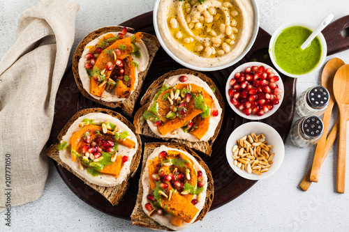 snack breads with hummus and baked pumpkin on a serving board with arugula pesto. seeds of pomegranate and pine nuts. healthy food