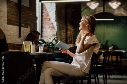 Young blond lady drinking coffe and looking aside through a window. in modern cafe interior.