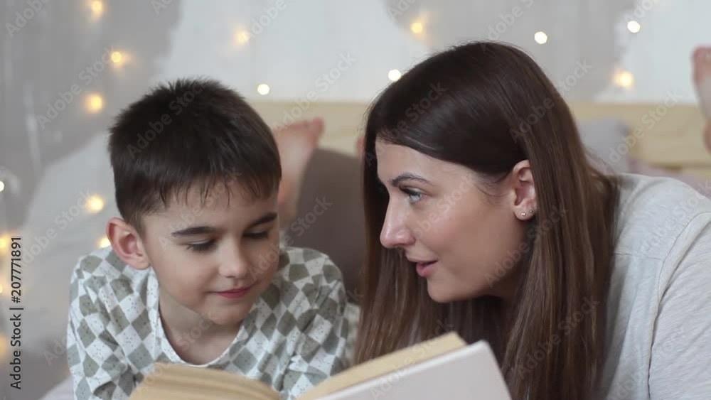 A beautiful girl with long hair reads a book to a small boy lying on a bed and kisses him. Close-up. HD A beautiful girl with long hair reads a book to a small boy lying on a bed and kisses him. Close-up. HD