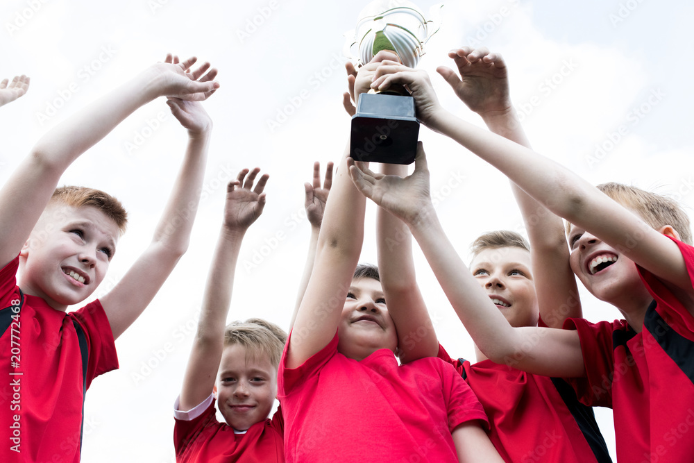 Obraz premium Low angle portrait of junior football team holding trophy together and cheering happily after winning match
