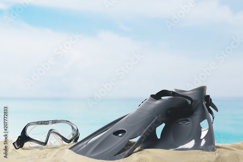 Mask and flippers in sand on blue sky background