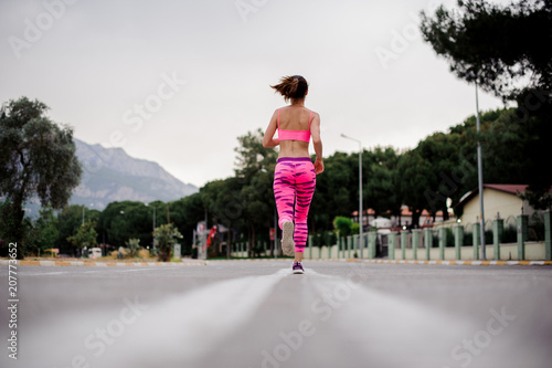 Back view of woman running along the highway in the morning