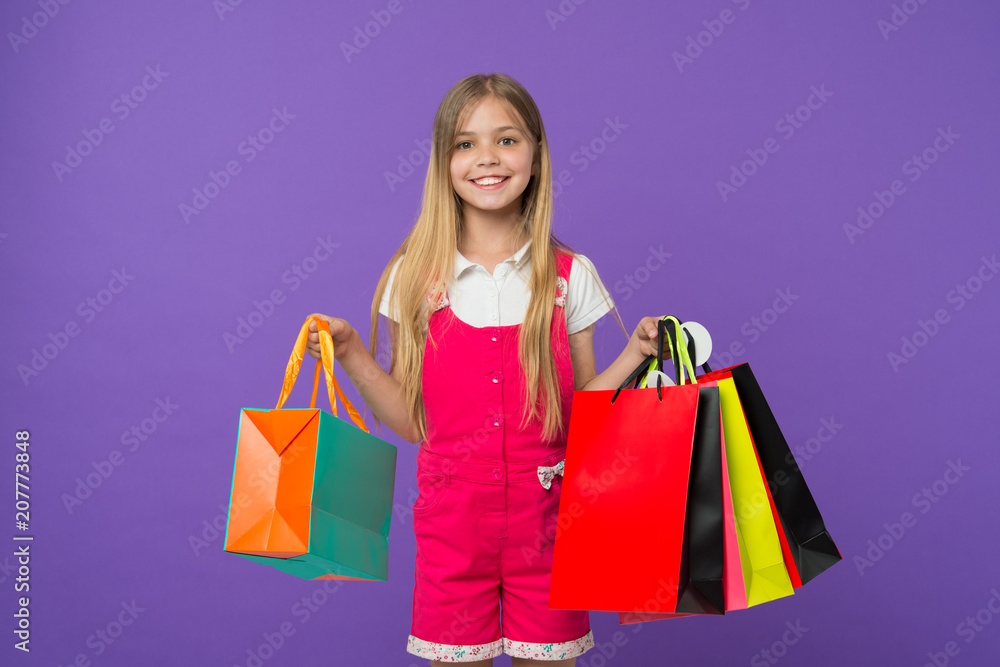 Girl on smiling face carries bunches of shopping bags, isolated on white background. Girl likes to buy fashionable clothes in shopping mall. Kid girl with long hair fond of shopping. Shopping concept Girl on smiling face carries bunches of shopping bags, isolated on white background. Girl likes to buy fashionable clothes in shopping mall. Kid girl with long hair fond of shopping. Shopping concept