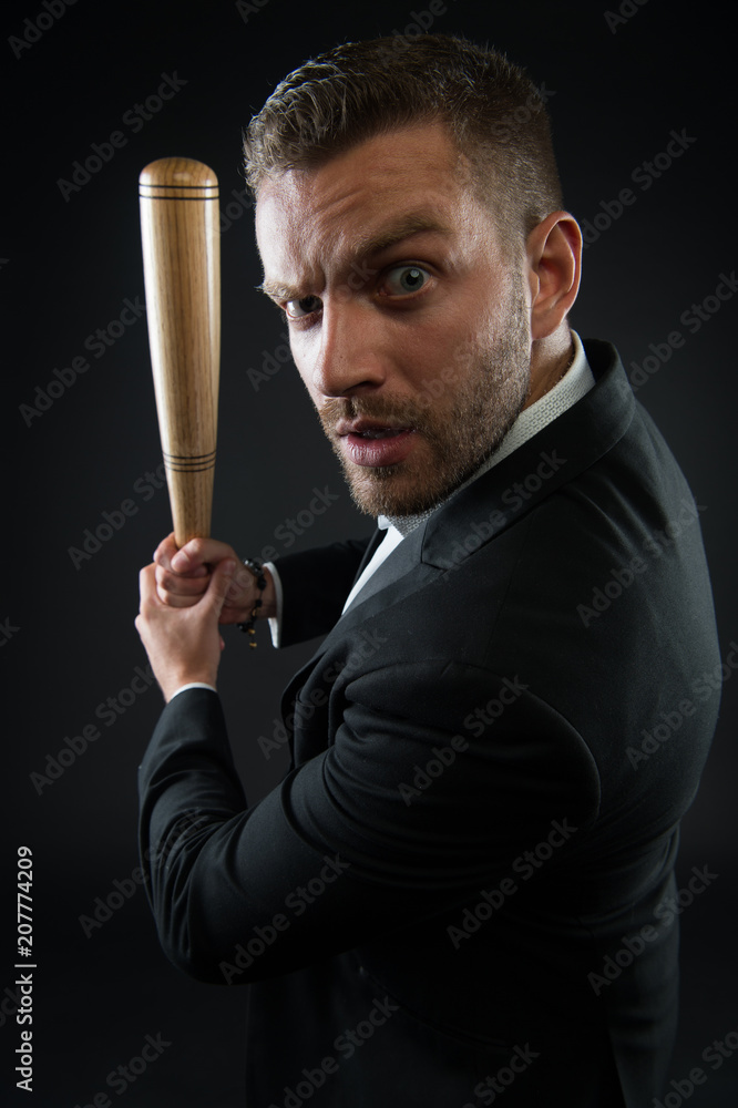 Businessman or man in formal suit on dark background. Man on strict face posing with wooden bat. Man with bristle looks confident and threatening. Aggressive business concept Businessman or man in formal suit on dark background. Man on strict face posing with wooden bat. Man with bristle looks confident and threatening. Aggressive business concept
