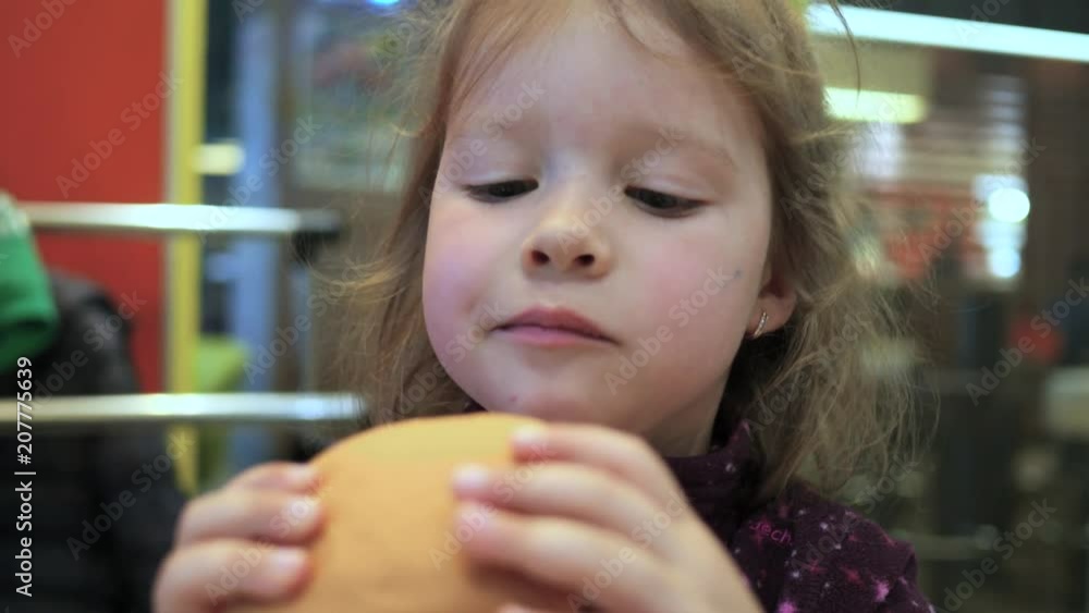 Little girl child eating a burger in a fast food restaurant Little girl child eating a burger in a fast food restaurant