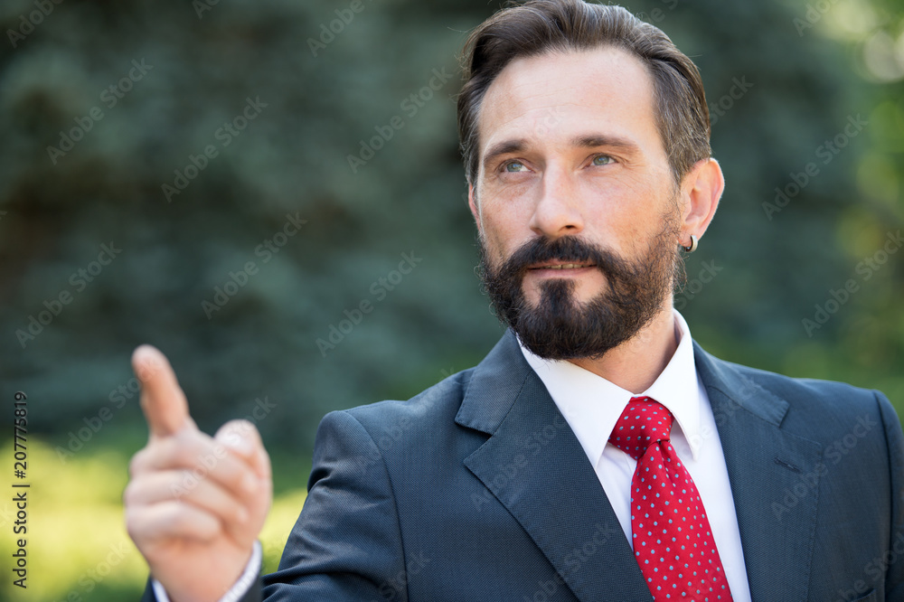 Handsome businessman point to the target in the future. Man in suit and red tie point hand forward over green outside background. Business success and target concepts.