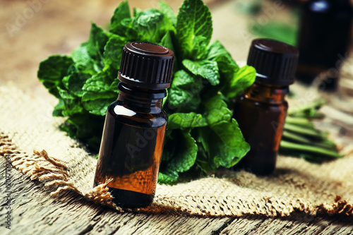 Fototapeta Naklejka Na Ścianę i Meble -  Essential oil of peppermint in a small brown bottle with fresh green mint, rustic style, vintage wooden background, selective focus