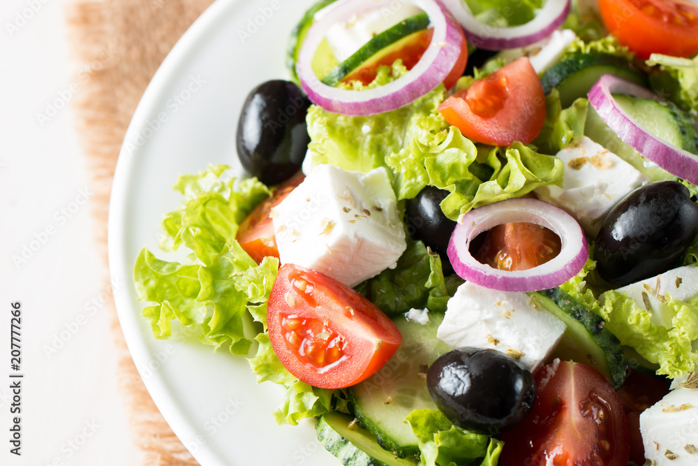 Fresh Greek salad made of cherry tomato, ruccola, arugula, feta, olives, cucumbers, onion and spices. Caesar salad in a white bowl on wooden background. Healthy organic diet food concept. Fresh Greek salad made of cherry tomato, ruccola, arugula, feta, olives, cucumbers, onion and spices. Caesar salad in a white bowl on wooden background. Healthy organic diet food concept.