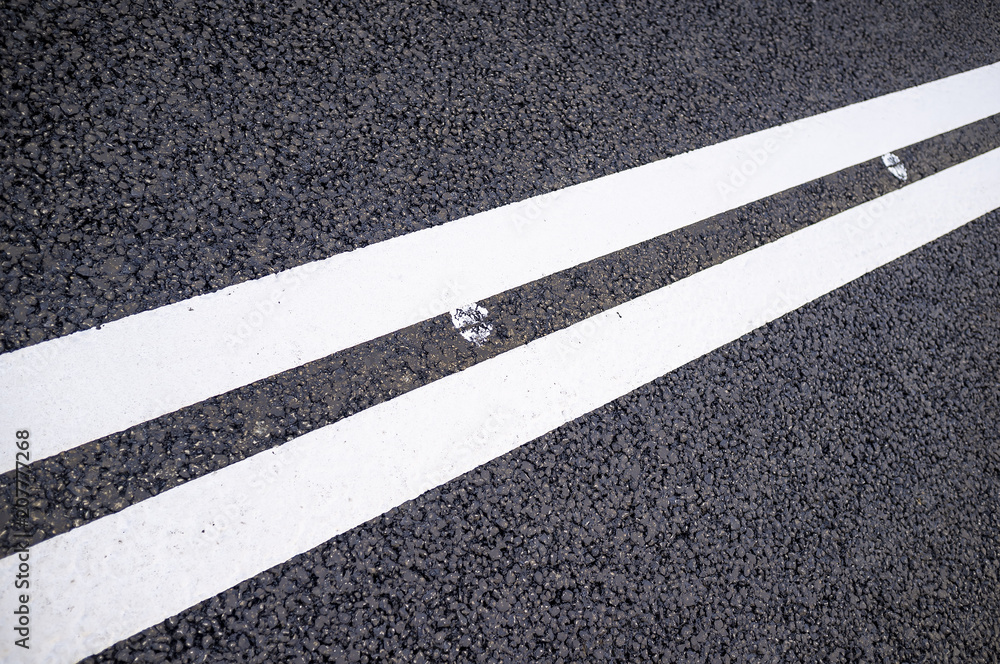 Fototapeta premium Two white solid lines on a new asphalt road. Close-up.