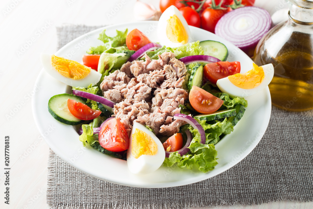 Fresh fish tuna salad made of tomato, ruccola, tuna, eggs, arugula, crackers and spices. Caesar salad in a white bowl on wooden background Fresh fish tuna salad made of tomato, ruccola, tuna, eggs, arugula, crackers and spices. Caesar salad in a white bowl on wooden background