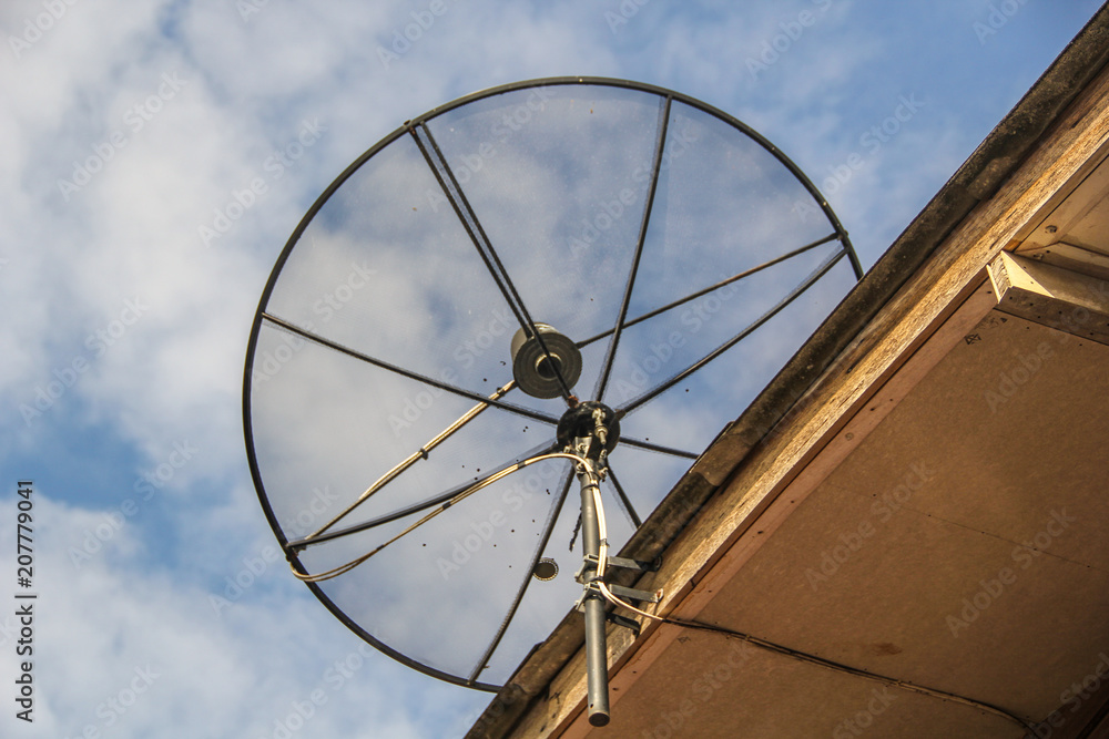 Satellite dish antenna for television on house roof with blue sky backgraund, in countryside, Thailand.