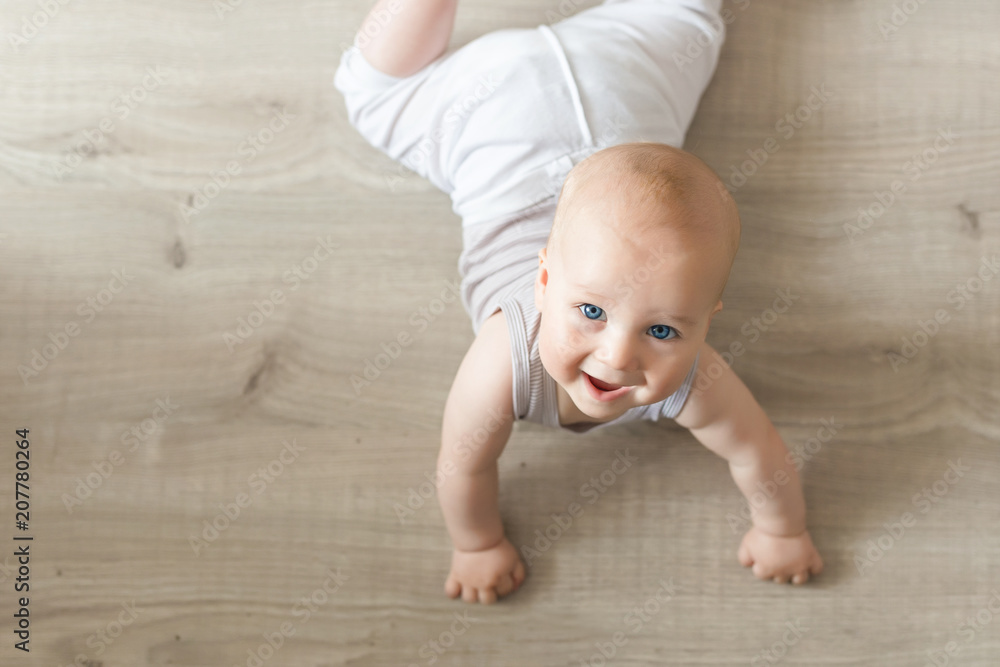 Cute little baby boy lying on hardwood and smiling. Child crawling over wooden parquet and looking up with happy face. View from above. Copyspace - obrazy, fototapety, plakaty 