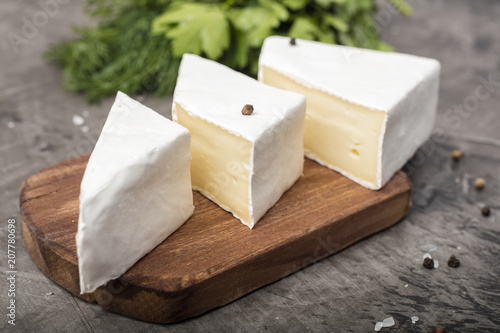 Three soft cheeses with white mold on a wooden cutting board