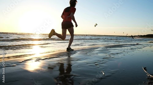 Man runs on the water at sea against the backdrop of kitesurfers at sunset, slow motion