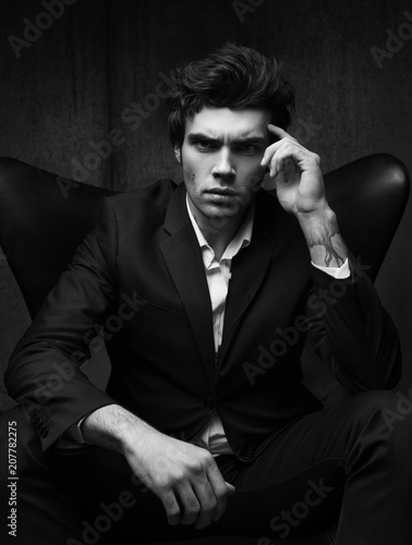 Black-and-white business portrait of a serious young man sitting in a chair.