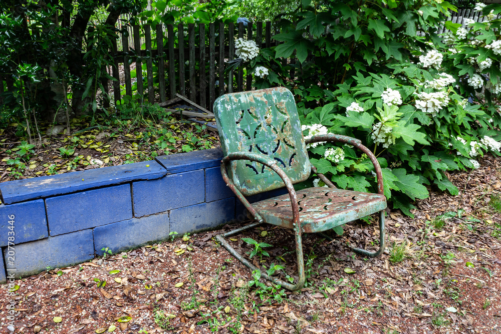 Empty green metal chair against a blue block wall, aging death grief absence concept, horizontal aspect