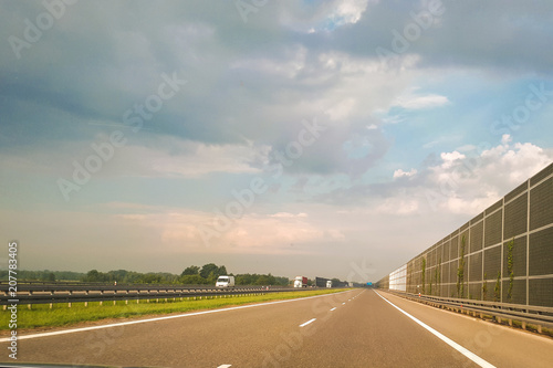 A view of the highway from the perspective of the driver and passenger. Dry asphalt, energy-intensive barriers and sky with clouds