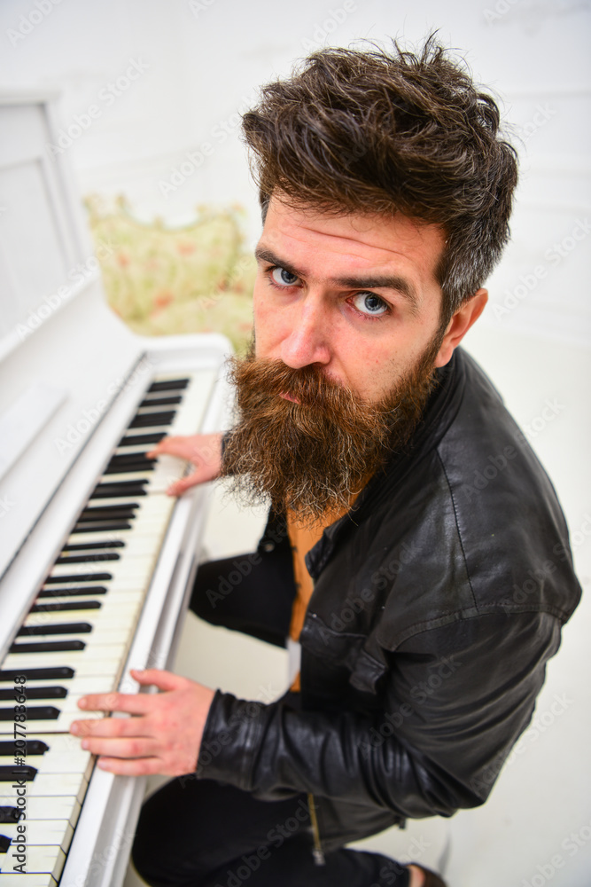 Fototapeta premium Talented musician concept. Man in leather jacket sits near piano musical instrument in white interior on background. Man, rock musician, pianist playing music on piano.